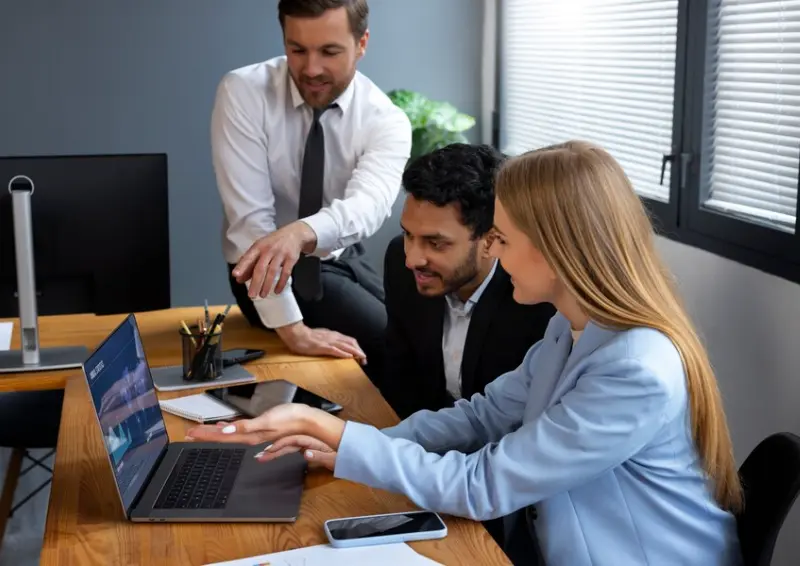 Three professionals reviewing data on a laptop in an office setting for a business directory profile